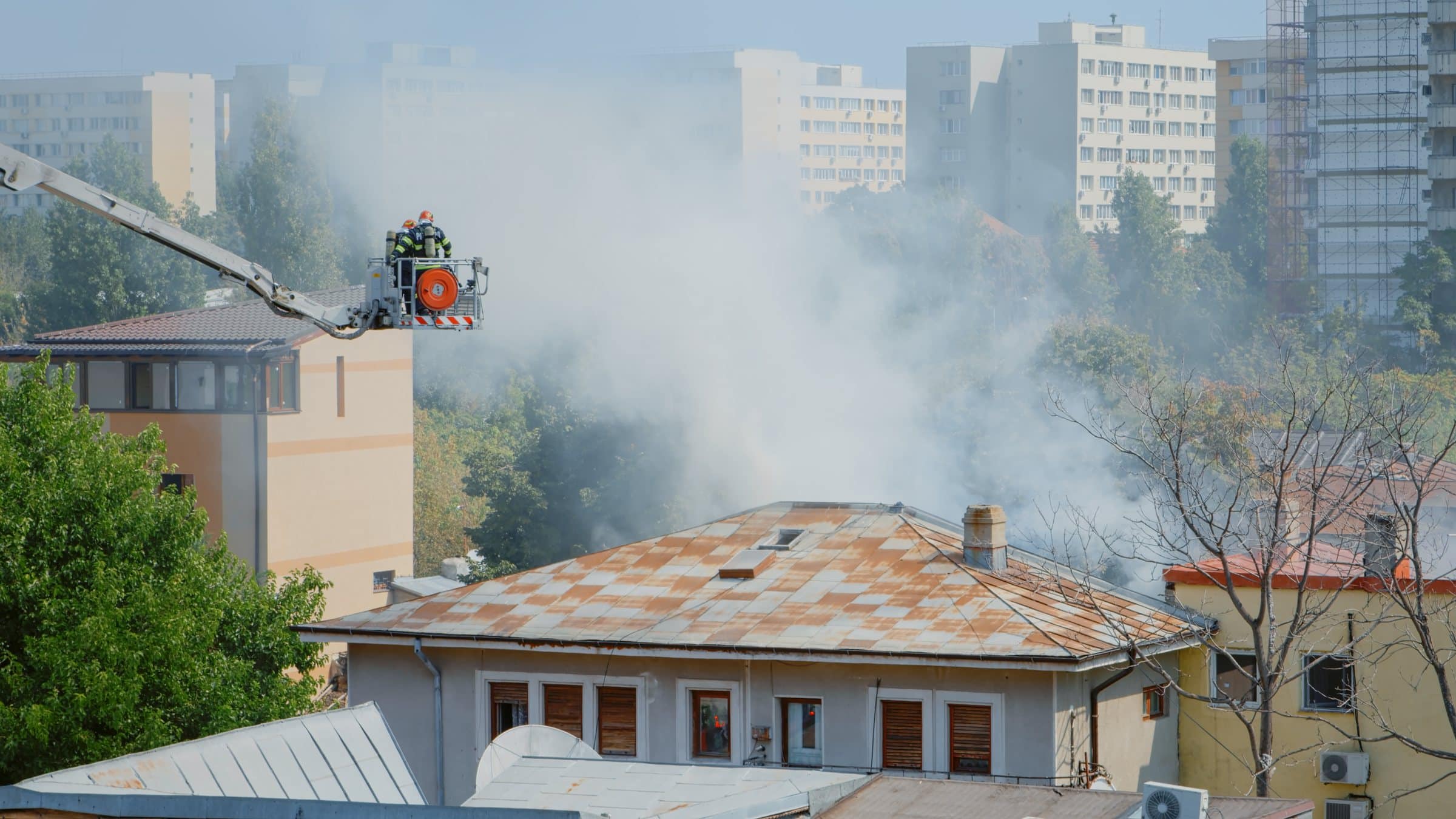Firefighters on a ladder truck spraying water on a burning roof