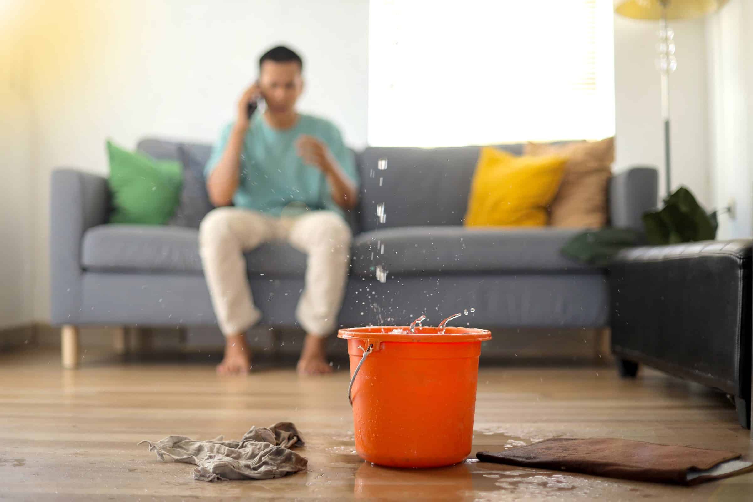 Homeowner on the phone while water drips from the ceiling into a bucket